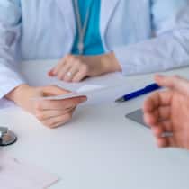 Mit diesen fünf Fragen finden Sie heraus, wie gut Ihr Arzt ist Unrecognizable doctor prescribing pills and drugs to patient. Male hand reaching for piece of paper with pharmacy recommendations. Symptom consultation and getting help