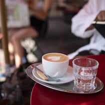 Happiger Aufpreis für Cappuccino mit Haferdrink Ein Cappuccino, zubereitet mit Haferdrink, steht auf einem Tisch eines Cafés.