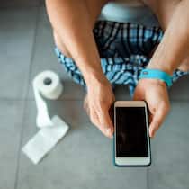 Nehmen Sie Ihr Smartphone nicht mit aufs WC! Close up of gentleman sitting on toilet bowl and holding smartphone stock photo