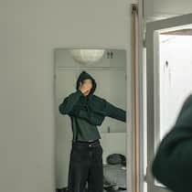 Thurgauer Gemeinden dürfen Eltern schröpfen 16-year-old young man is dressing up in front of the mirror in his sleeping room. He is a handsome fair-haired boy and he sets his hair so that he is ready to go out. He is wearing a dark green hoodie. He covers his face with his hand.