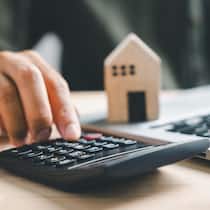 Festhypothek oder Saron? So hat sich die Ausgangslage geändert Pressing calculators, hand eyes home refinance. Wooden house model, buy/rent note on desk. Saving for property purchase concept, efficient mortgage payment. Tax, credit analysis for financial strategy
