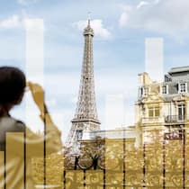 Kurztrip geplant? So reisen Sie am günstigsten, schnellsten und grünsten Frau, Touristin, in der Unschärfe von hinten mit Blick auf den Eifelturm in Paris. Herbststimmung.Mit Balkendiagramm halbtransparent, Infografik zu den verschiedenen Kosten zu Bahn, Auto, Velo bei einem Kurztrip nach Paris, San Remo oder Appenzell.