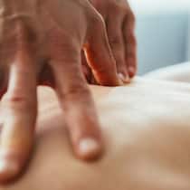 Osteopath bricht Frau Rippe – und verklagt sie Nahaufnahme von Händen, die den Rücken einer Person massieren.