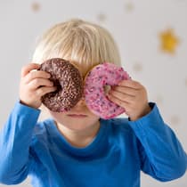 Kinder sollen weniger Werbung für Junkfood sehen Kind hält Donuts vor die Augen - Werbung für besonders süsse, salzige und fettige Produkte an Kinder soll ab 2027 eingeschränkt werden. Noch ist die Regelung aber nicht unter Dach