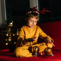 Gemeinsam oder getrennt feiern? So gelingt das Weihnachtsfest Ein kleiner Junge in einem gelben Pyjama sitzt auf einem roten Sofa neben einem Weihnachtsbaum und packt ein Geschenk aus - Wenn getrennte Paare Weihnachten mit Kindern feiern, stellt sich die Frage, ob sie die Feiertage gemeinsam oder getrennt begehen sollen. Das rät die Beobachter-Expertin für Familienrecht.