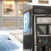Das grosse Parkplatz-Abc Im Vordergrund sieht man eine Parkuhr und im Hintergrund ist ein parkiertes Auto.