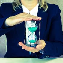 Was in der Privatwirtschaft rechtlich gilt Eine Frau in Business-Kleidung hält vor sich eine Sanduhr in der Hand.