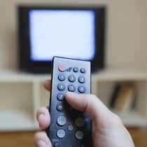 Sind wir von den Radio- und TV-Gebühren befreit? Eine Person hält eine Fernbedienung in der Hand. Im Hintergrund sieht man etwas verschwommen ein TV-Gerät.