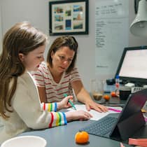 Die Kinder zu Hause unterrichten? Eine Mutter arbeitet im Homeoffice und kümmert sich nebenbei um ihre kleine Tochter, die ihre Schulaufgaben macht.