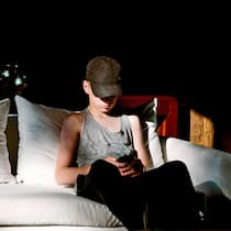 Dürfen Eltern bei Verdacht rumstöbern? Ein minderjähriger Junge sitzt auf dem Sofa in einem verdunkelten Zimmer und sieht sich heimlich Bilder auf seinem Handy an. Wenn es um den Besitz von Nacktbildern Minderjähriger geht, kennt das Gesetz kein Pardon. Dennoch sollten Eltern bei einem Verdacht nicht einfach das Handy kontrollieren.