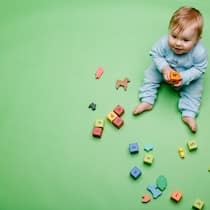 Kindersachen mieten statt kaufen Baby sitzt mit Spielsachen da.