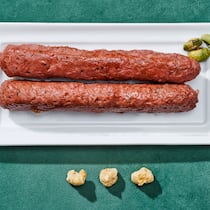 Ab fünf Zutaten wirds kritisch Zwei Cevapcici auf einem Teller auf grünem Untergrund. Warum ultrahochverarbeitete Lebensmittel ungesund sind