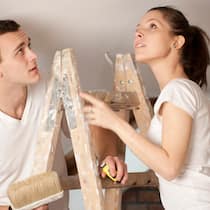 Welche Schäden müssen Mieter zahlen? Junges Paar steht auf einer Leiter und trifft Vorbereitungen, um anschliessend die Decke neu anzustreichen