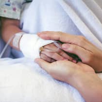 Bekommt man frei, wenn das Kind krank ist? Ein kleines Kind liegt in einem Spitalbett, die Mutter hält ihre Hand in ihren.