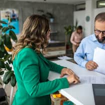 Wieso erbe ich die Säule 3a meiner Tante nicht? Eine Bankkundin steht am Bankschalter und lässt sich ihre Dokumente durch einen Angestellten prüfen.