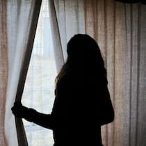 Schweizer Frauenhäuser platzen aus allen Nähten Frau schaut aus dunklem Raum zum Fenster raus - Die Gewalt in den eigenen vier Wänden nimmt zu – gleichzeitig gibt es zu wenig sichere Orte für Betroffene. Die Frauenhäuser in der Schweiz arbeiten am Limit