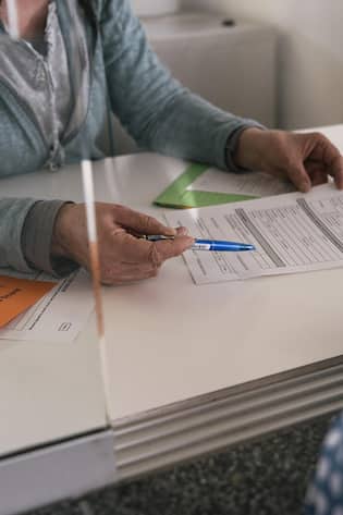 Beamtin zeigt auf ein Formular - Kommentar: Wer im Kanton St. Gallen lebt, muss bezogene Gelder später teils vollständig zurückzahlen – in Zürich keinen Rappen. Diese Lotterie ist unfair und gehört abgeschafft