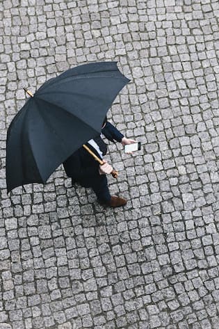 Mann mit Handy unter einem Regenschirm - Wer Missstände aufdeckt, verliert in der Schweiz oft seinen Job und wird diffamiert. Zwei Fälle zeigen, warum wir die Überbringer schlechter Nachrichten dringend schützen müssen
