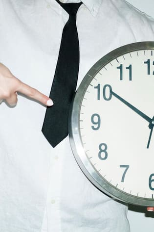 Person wearing office work shirt and tie holding and pointing a clock with hard direct flash
