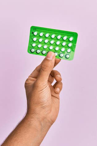 Young hispanic hand holding birth control pills over isolated pink background.