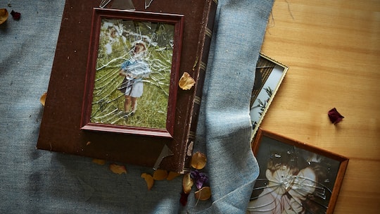 Ein Bild in einem Bilderrahmen mit zerbrochenem Glas liegt auf einem Tisch, auf dem Bild sieht man eine Person.