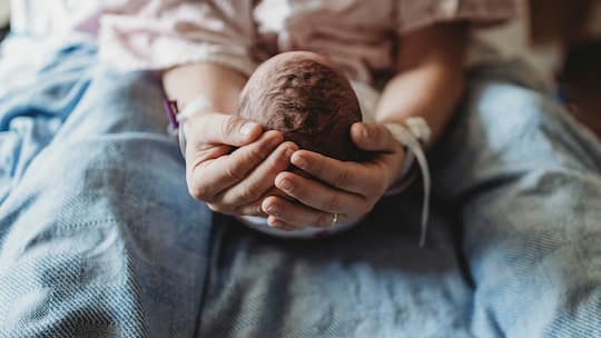Neugeborenes Kind in den Händen einer erwachsenen Person;