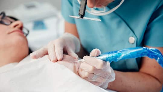 Eine Frau liegt auf einem Behandlungstisch und wird von einer medizinischen Fachperson an der Brust tätowiert, um eine Brustwarze nachzustellen.