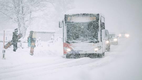 Bus im Schneegestöber. Snowboarder steigen ein.