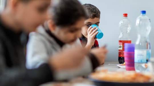 Junge trinkt aus Plastikbecher und sitzt mit seiner Familie am Esstisch in der Asylunterkunft. Ein Drittel aller Asylgesuche in der Schweiz kommt von Kindern