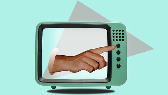 Ein alter grüner Fernseher aus dem eine Hand mit erhobenem Zeigefinger zeigt.