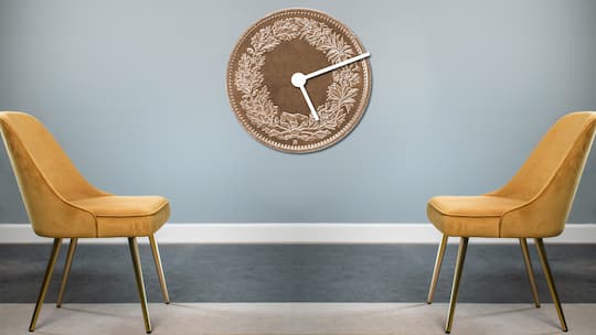Zwei bequeme Sessel stehen sich gegenüber, dazwischen hängt eine Uhr an der Wand. Das Ziffernblatt ist eine Münze.