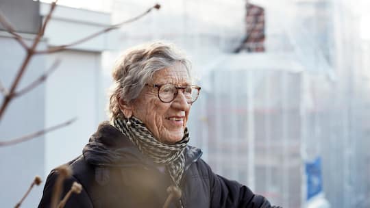Eine ältere fitte Frau mit kurzen grauen Haaren und Brille schaut leicht lächelnd an der Kamera vorbei.