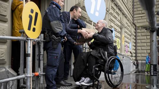 Eine Person im Rollstuhl uebergibt eine Schachtel mit Unterschriften auf einer speziell installierten Rampe, waehrend der Uebergabe der Inklusions-Initiative an die Bundeskanzlei, am Donnerstag, 5. September 2024 vor der Bundeskanzlei, in Bern. Die Initiative verlangt die Gleichstellung von Menschen mit und ohne Behinderungen in allen Lebensbereichen. (KEYSTONE/Anthony Anex)