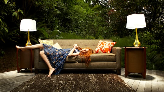 Eine junge Frau liegt auf einem Sofa, welches sich zusammen mit anderen Einrichtungsgegenständen in einem Wald befindet. Bei einer Ausweisung aus der Wohnung dürfen Vermieter ihre Mieter nicht einfach auf die Strasse stellen. So gehen Vermieterinnen anstattdessen vor, wenn die Mieterin trotz Kündigung nicht ausziehen will.