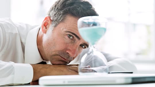 Gelangweilter Buerolist schaut auf Sanduhr