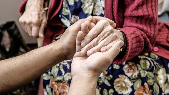 Eine Pflegerin hält die Hand einer Seniorin.