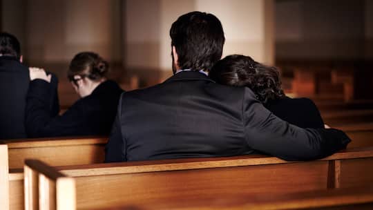 Todesfallversicherung, eine Familie sitzt bei der Beerdigung in der Kirche