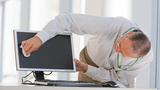 Ein älterer Mitarbeiter reinigt seinen Comupterbildschirm.