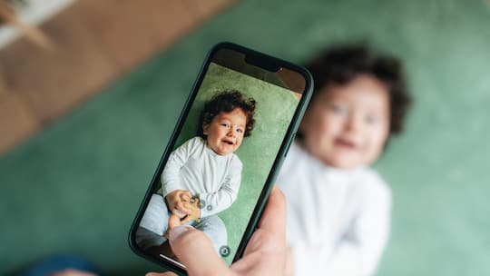 Frau macht mit Handy einen Schnappschuss von einem Kind - Ein Lächeln auf Facebook, Konsequenzen Jahre später. Was Eltern über die Langzeitfolgen von Kinderfotos online wissen sollten