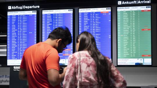 Zwei Flugpassagiere erkundigen sich via Handy und Anzeigetafel über ihren Flug, nachdem die Flugsicherung Skyguide den Luftraum über der Schweiz am frühen Vormittag des 15. Juni 2022 wegen einer technischen Störung im Netzwerk sperrte.