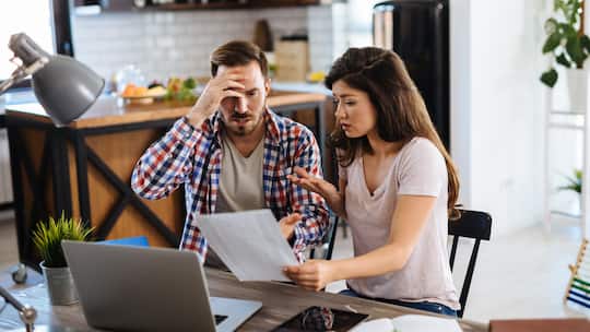 Ein Paar sitzt am Küchentisch und diskutiert mit besorgter Miene über offene Rechnungen.