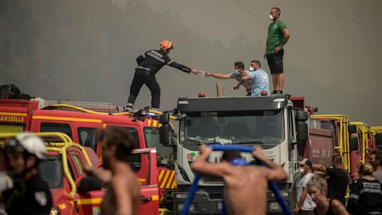 Ein Feuerwehrmann reicht einem freiwilligen Helfer eine Atemschutzmaske, während sie am 29. Juli 2026 einen Waldbrand in Lanton, östlich der Bucht von Arcachon und westlich von Bordeaux, bekämpfen.