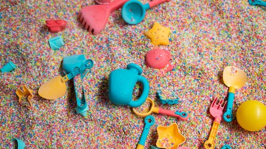 Farbiges Plastikspielzeug im Sand, teils vergraben