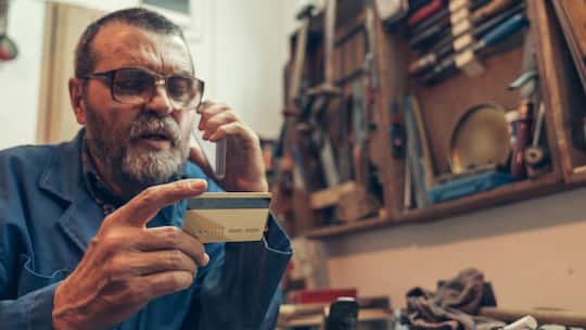 Senior man in the workshop holding credit card and talking by phone