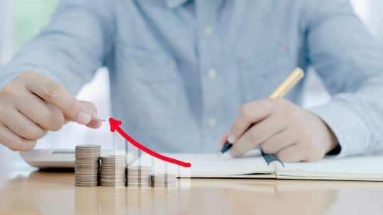 Eine Person sitzt an einem Tisch und studiert Unterlagen. Vor ihr liegen Münzen aufgereiht.