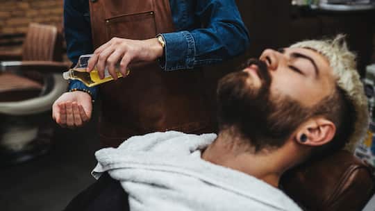 Ein Kunde liegt auf einem Friseurstuhl in einem Barbershop und lässt sich seinen Bart mit einem kosmetischen Öl behandeln. Genau in solchen Bartpflegeprodukten wurden Inhaltsstoffe gefunden, die Allergien auslösen können und teils gar verboten sind.
