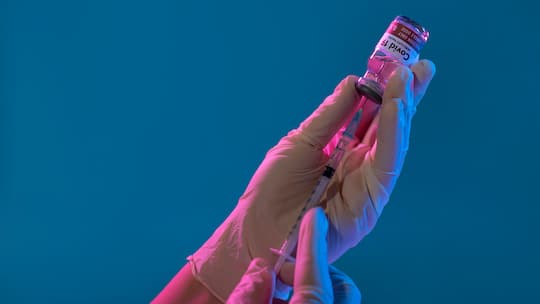 Bild einer medizinischen Fachperson, die eine Dosis eines Corona-Impfstoffs in einer Spritze aufzieht.