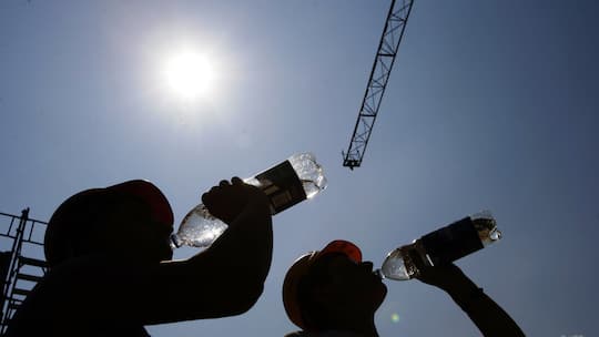 Zwei Bauarbeiter trinken aus Wasserflaschen. Hohe Temperaturen machen die Arbeit beschwerlich. Wer kann hitzefrei machen? Eine Übersicht.