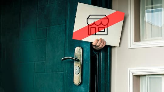 Eine Person hält ein Schild aus der Haustüre, auf dem ein rot durchgestrichener Verkaufsladen zu sehen ist.