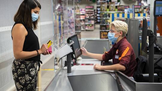 Kundin mit Schutzmase bezahlt an der Migros-Kasse